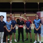 Seven men pictured standing in front a football stadium, looking to camera