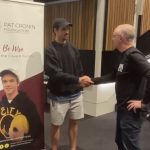 Two men talking and shaking hands in front of a Pat Cronin Foundation banner, profile shot