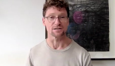 Man wearing glasses and t-shirt ion front of a painting on a wall